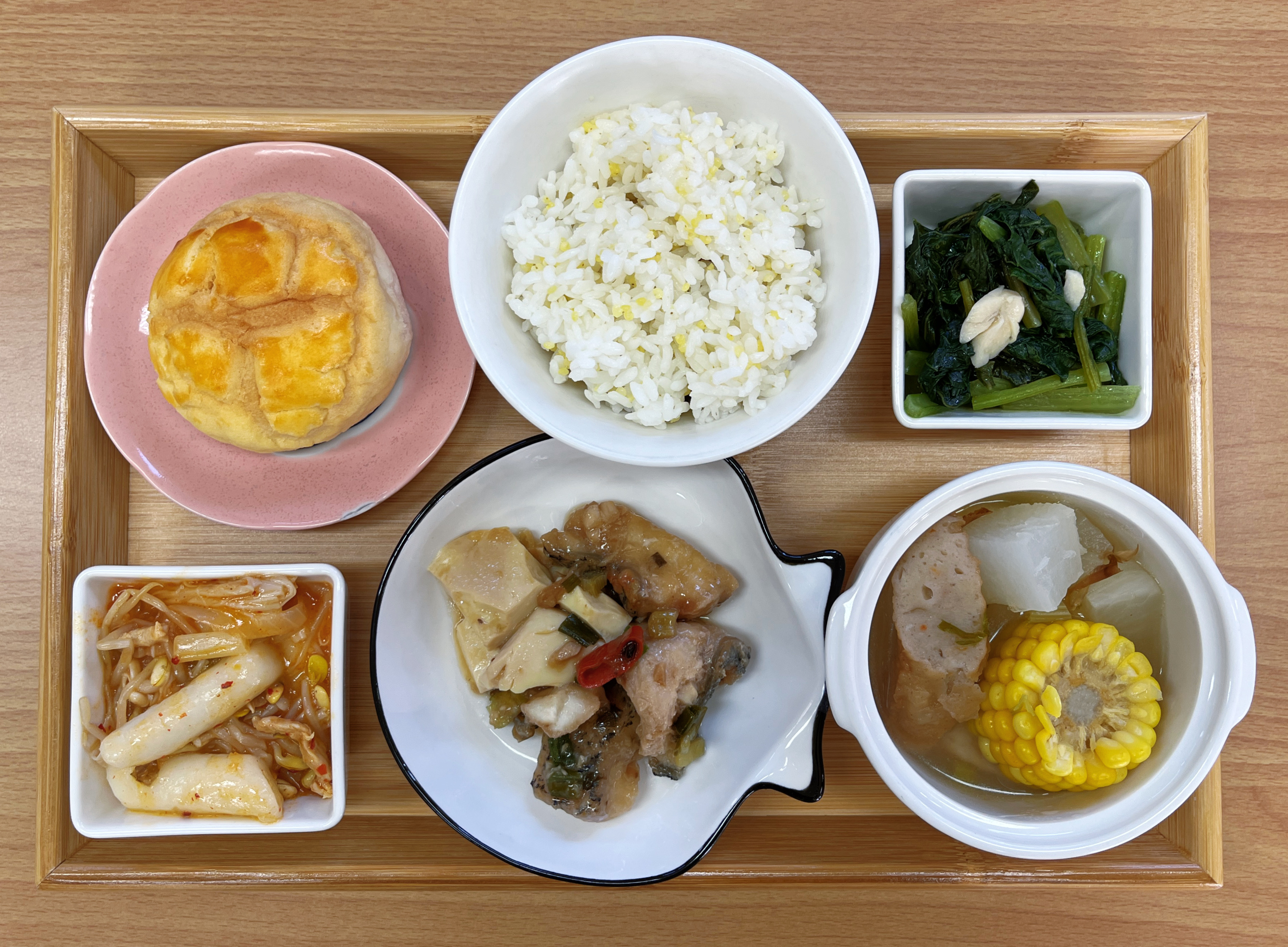 Actual Week 8 Tuesday school lunch tray with kimchi stir-fried rice cakes in a small dish, rice, leafy greens, a stir-fried main dish, a side dish and a bowl of soup with corn